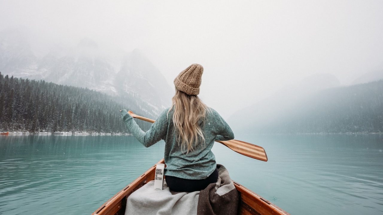 woman in gray long sleeve shirt sitting on brown wooden boat on body of water during