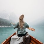 woman in gray long sleeve shirt sitting on brown wooden boat on body of water during