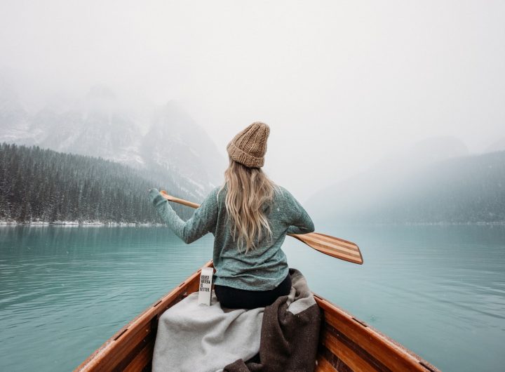 woman in gray long sleeve shirt sitting on brown wooden boat on body of water during
